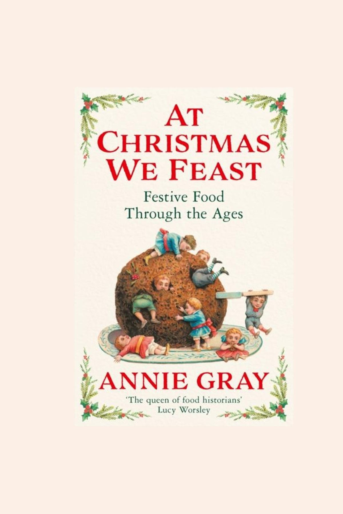 Book cover of 'At Christmas We Feast' by Annie Gray with a vintage illustration of children around a Christmas pudding.