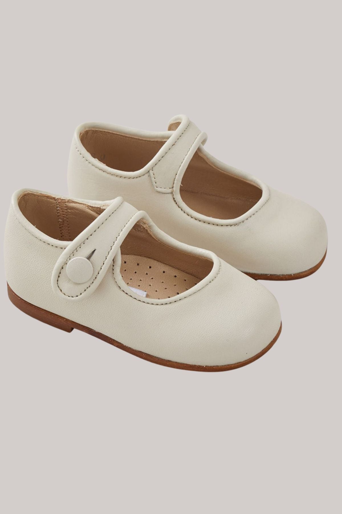 Pair of cream-coloured children's shoes with a strap on a light gray background