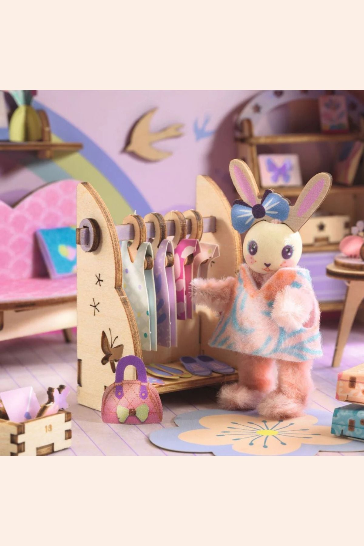 Toy rabbit character in a dress standing next to a wooden dress-up rack with clothes in a colourful room.