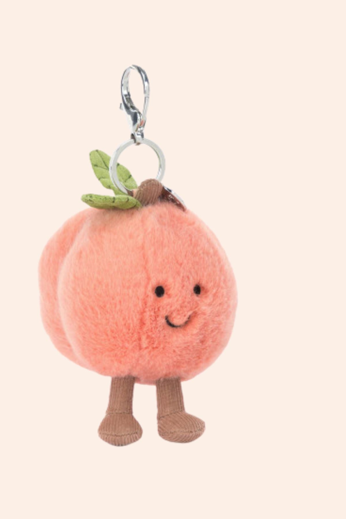 Plush peach charm with legs and a smiling face on a beige background