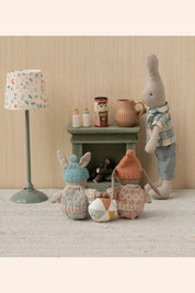 Three toy rabbits in a room with a lamp and small table.