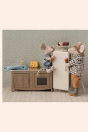 Two toy mice in a kitchen setting with a refrigerator and cabinets.