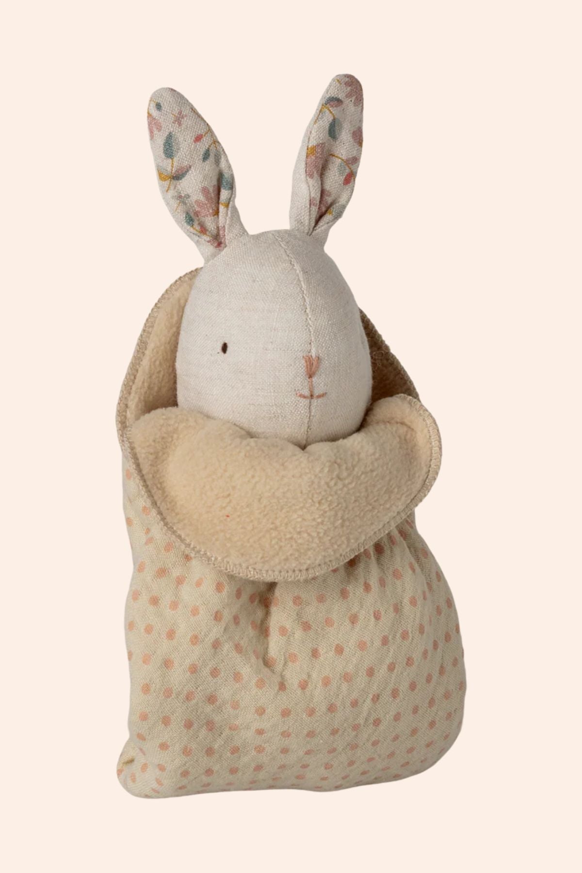 Stuffed rabbit toy in a patterned bag on a beige background