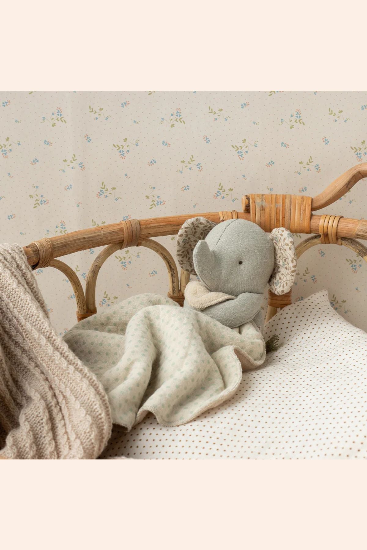 Gray elephant plush toy in a crib with a floral-patterned wall in the background