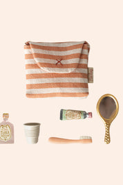 Collection of travel-sized toiletries including a striped pouch, bottle, cup, brush, and mirror on a white background.