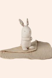 White plush rabbit toy on a beige blanket with a white background
